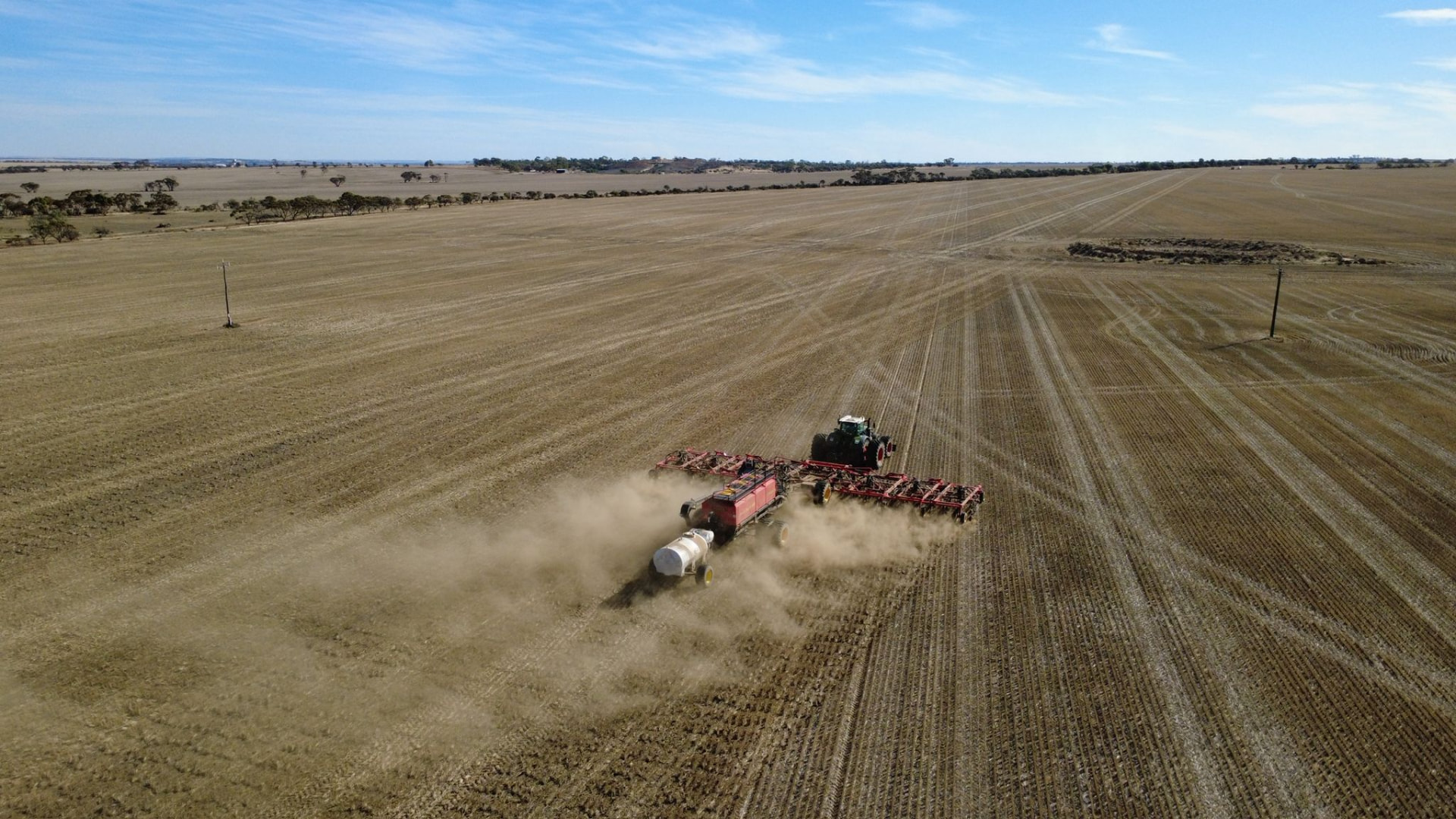 Wide Western Australian cropping country with a seeding rig raising dust